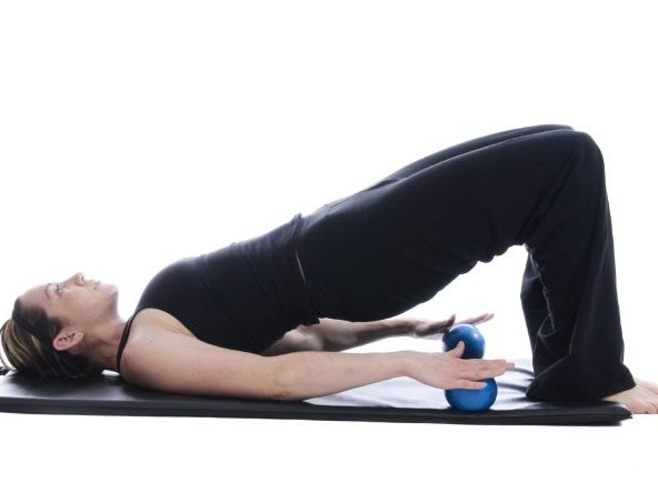 Frau in Rückenlage, führt eine Brücke mit Hanteln in den Händen aus.