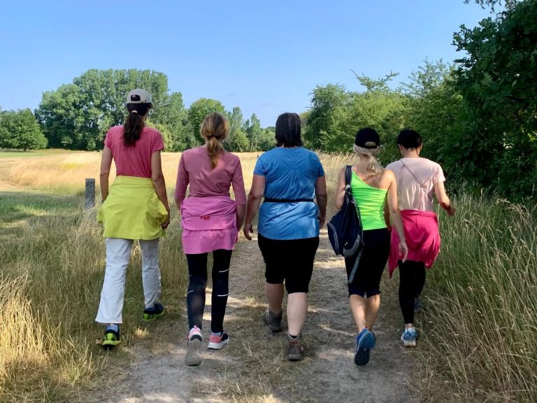 Grupp von fünf Frauen geht auf einem Wanderweg in der Natur.