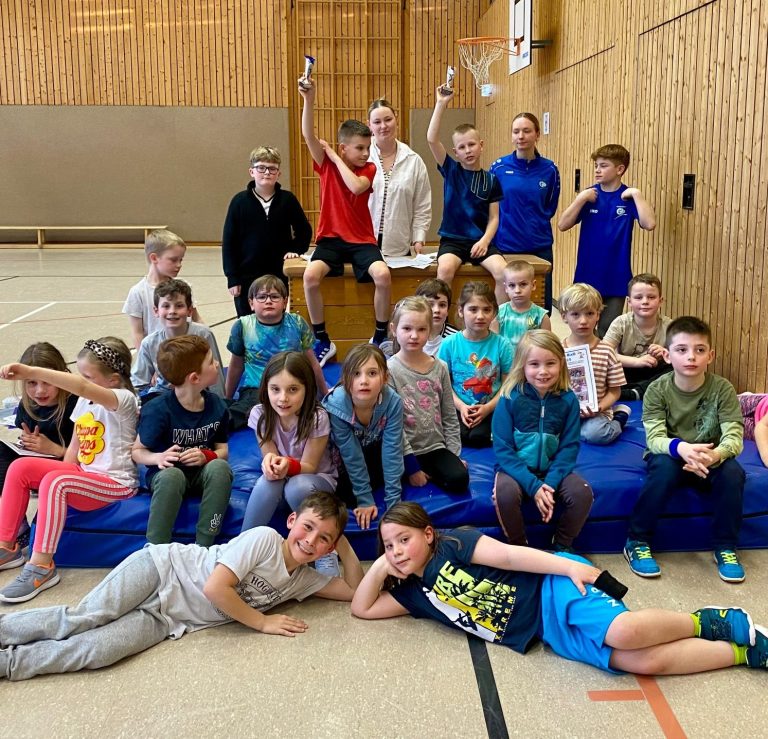 Gruppe von Kindern und Betreuern in einer Sporthalle, alle lächeln und posieren.